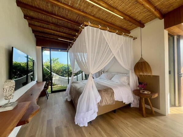 A bedroom with a canopy bed, a wooden bench, a TV, and a view of greenery outside. - UMBELINA POUSADA BOUTIQUE (Ipojuca)