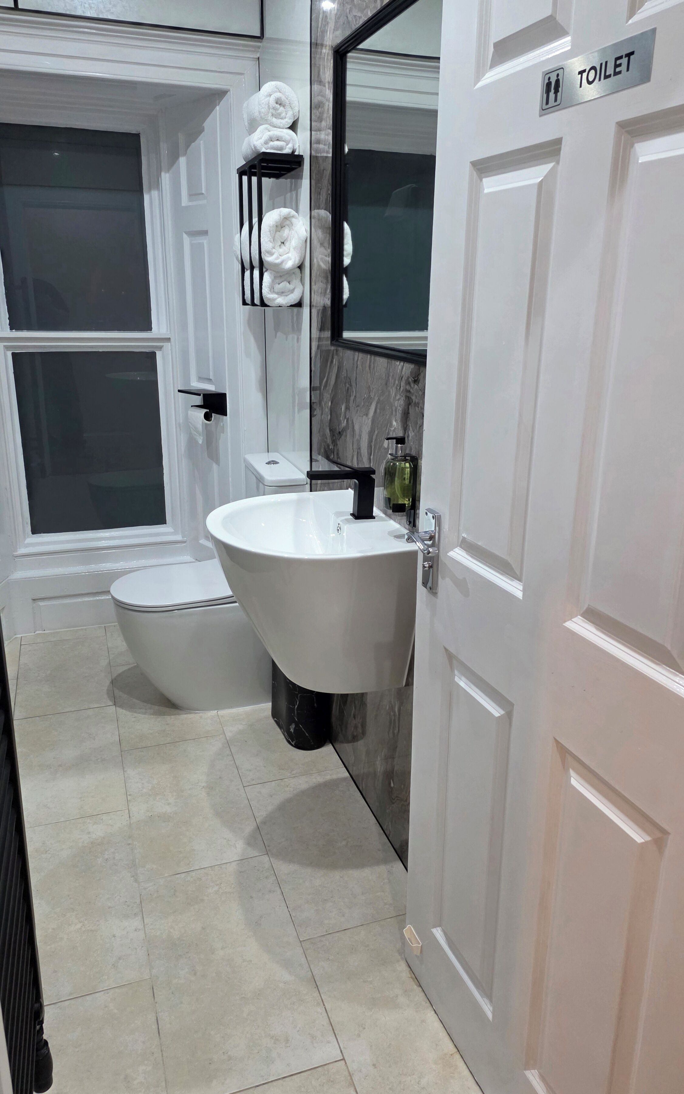 Een moderne badkamer met toilet, wastafel en een handdoekrek met handdoeken.