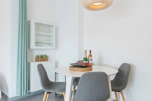 Ein Essbereich mit einem runden Tisch, grauen Stühlen, einer gewebten Tischmatte und einem an der Wand befestigten Schrank mit Gläsern.