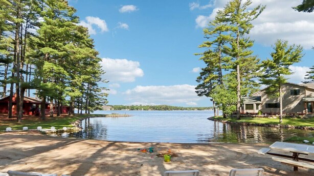 A lakeside property with a sandy beach, lounge chairs, and a view of the lake. - Johnny`s Lucky 13 at Island Pointe (Wisconsin Dells)