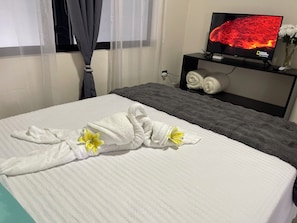 Habitación de hotel con una cama, un televisor sobre un mueble y una ventana con cortinas.