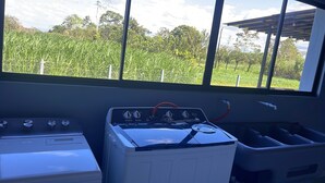 A kitchen with a stove, a washing machine, and a window with a view of a green field. - Charming 2-bedroom villa with AC in peaceful  de La Fortuna, San Carlos (San Carlos)
