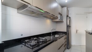 A modern kitchen with a gas stove, stainless steel appliances, and white cabinetry. - Fully Equipped Apartments in the Condo With Pool in Canasvieiras - RPC (Florianópolis)