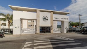 A building with a sign reading "PORTO CARAVELAS" and a logo above the entrance. - Fully Equipped Apartments in the Condo With Pool in Canasvieiras - RPC (Florianópolis)
