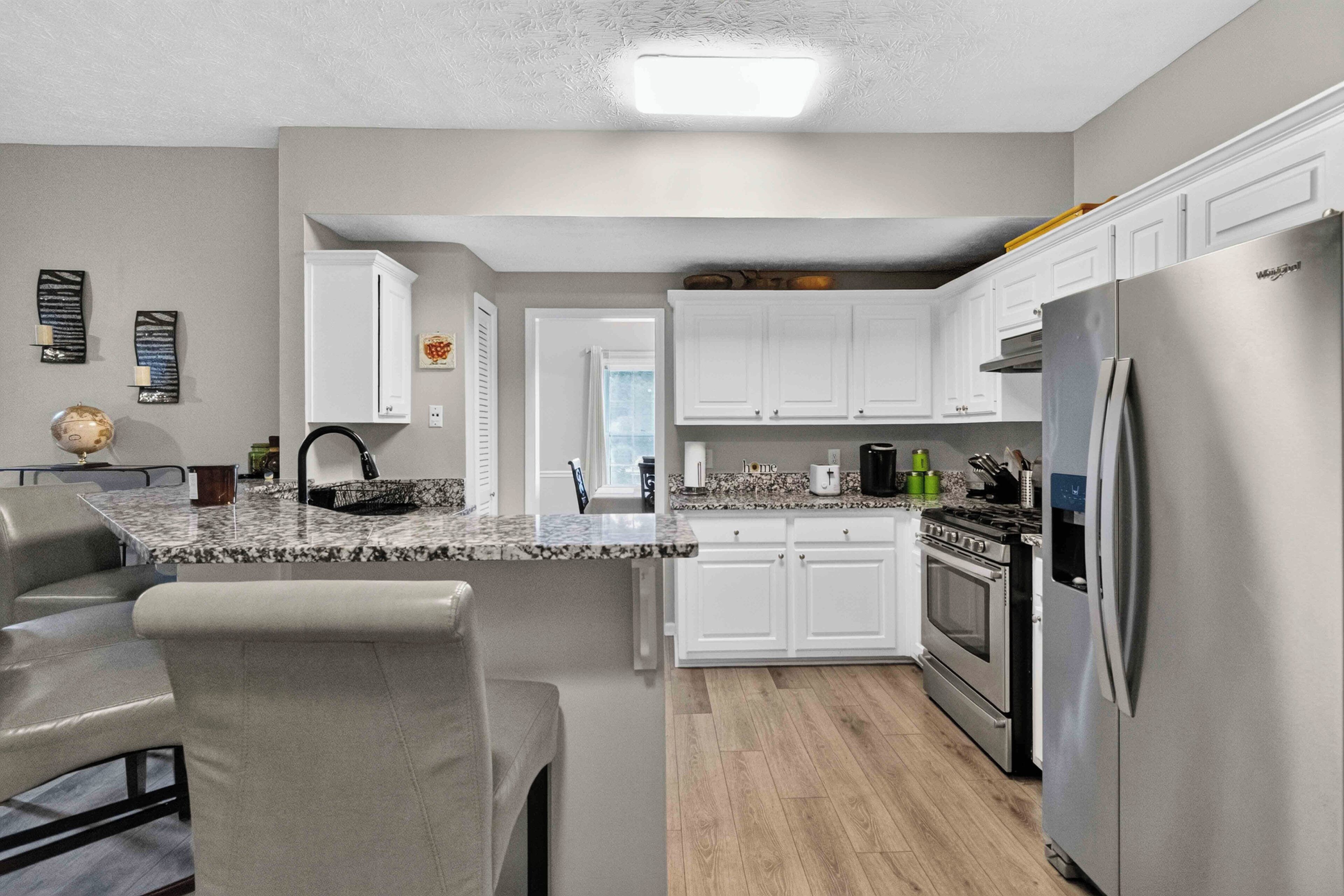 Una cocina moderna con armarios blancos, un refrigerador de acero inoxidable y una encimera de granito.