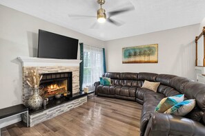 A living room with a fireplace, a leather sofa, and a flat-screen TV mounted above the fireplace. - Fabulous 4BR Home, Office, Game Room & Deck/Huge Lawn (Conyers)