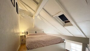 A small, sloped-roofed room with a single bed, a small window, and a white railing. - Duplex apartment in the center of Metz (Metz)