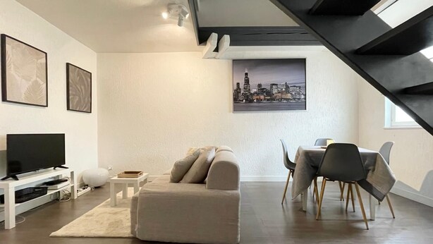A modern living room with a sofa, TV, dining area, and a cityscape painting. - Duplex apartment in the center of Metz (Metz)