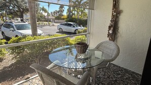 Une table à plateau en verre, des chaises en osier, un ventilateur de plafond et un élément décoratif mural.