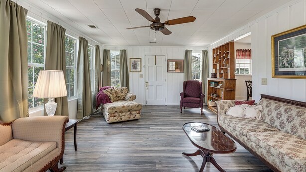 A spacious living room with a ceiling fan, a floral sofa, a wooden coffee table, and a bookshelf. - 2-Acre Farmhouse w/ Animals! Allendale Retreat (Allendale)