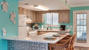 A kitchen with teal walls, wooden cabinets, a white island, and a dining area with wicker chairs. - Walk to Shore: Townhome w/ Pool Access in PCB! (Panama City Beach)