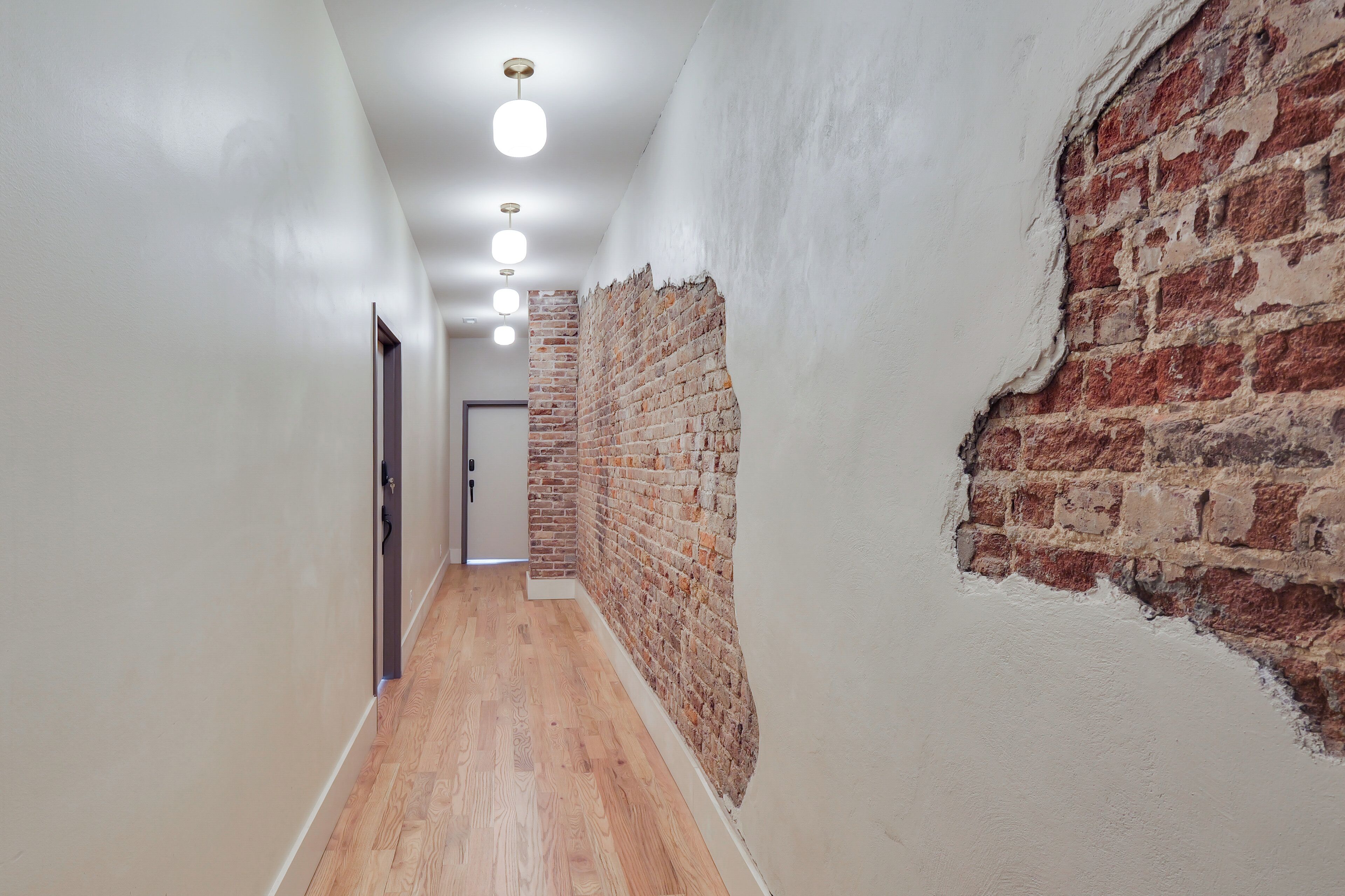 A hallway with a brick wall, wooden floor, and recessed lighting.