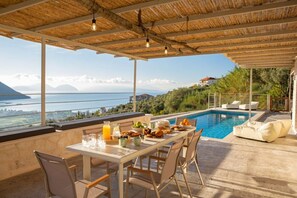 A terrace with a pool, dining table, chairs, and a view of the sea and mountains. - Ponti Monti - Two Bedroom Villa, Sleeps 4 (Vasiliki)