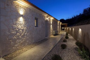A stone building with a pathway leading to a covered area, illuminated by wall-mounted lights. - Ponti Monti - Two Bedroom Villa, Sleeps 4 (Vasiliki)