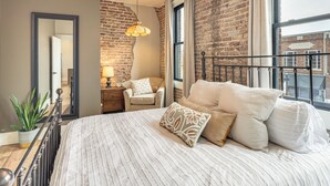 Une chambre avec un grand lit, un miroir, une chaise, un luminaire suspendu et un mur en briques.