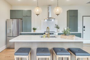 A modern kitchen with a central island, stainless steel appliances, green cabinets, and pendant lighting. - On Dtwn Square! Chic Lawrenceburg Condo w/ Balcony (Lawrenceburg)