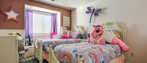 A bedroom with two beds, a ceiling fan, a star decoration, a butterfly wall art, and a window with purple curtains.