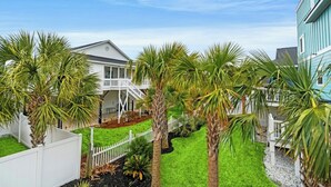 A residential area with a house, a white fence, and palm trees. - Coastal Serenity-3BR Luxury Home in Cherry Grove (North Myrtle Beach)