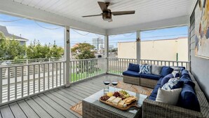 A covered outdoor area with a ceiling fan, a sofa with cushions, and a table with a cheese platter and glasses. - Coastal Serenity-3BR Luxury Home in Cherry Grove (North Myrtle Beach)