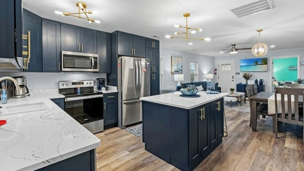 A modern kitchen with dark cabinetry, stainless steel appliances, and a marble island. - Coastal Serenity-3BR Luxury Home in Cherry Grove (North Myrtle Beach)