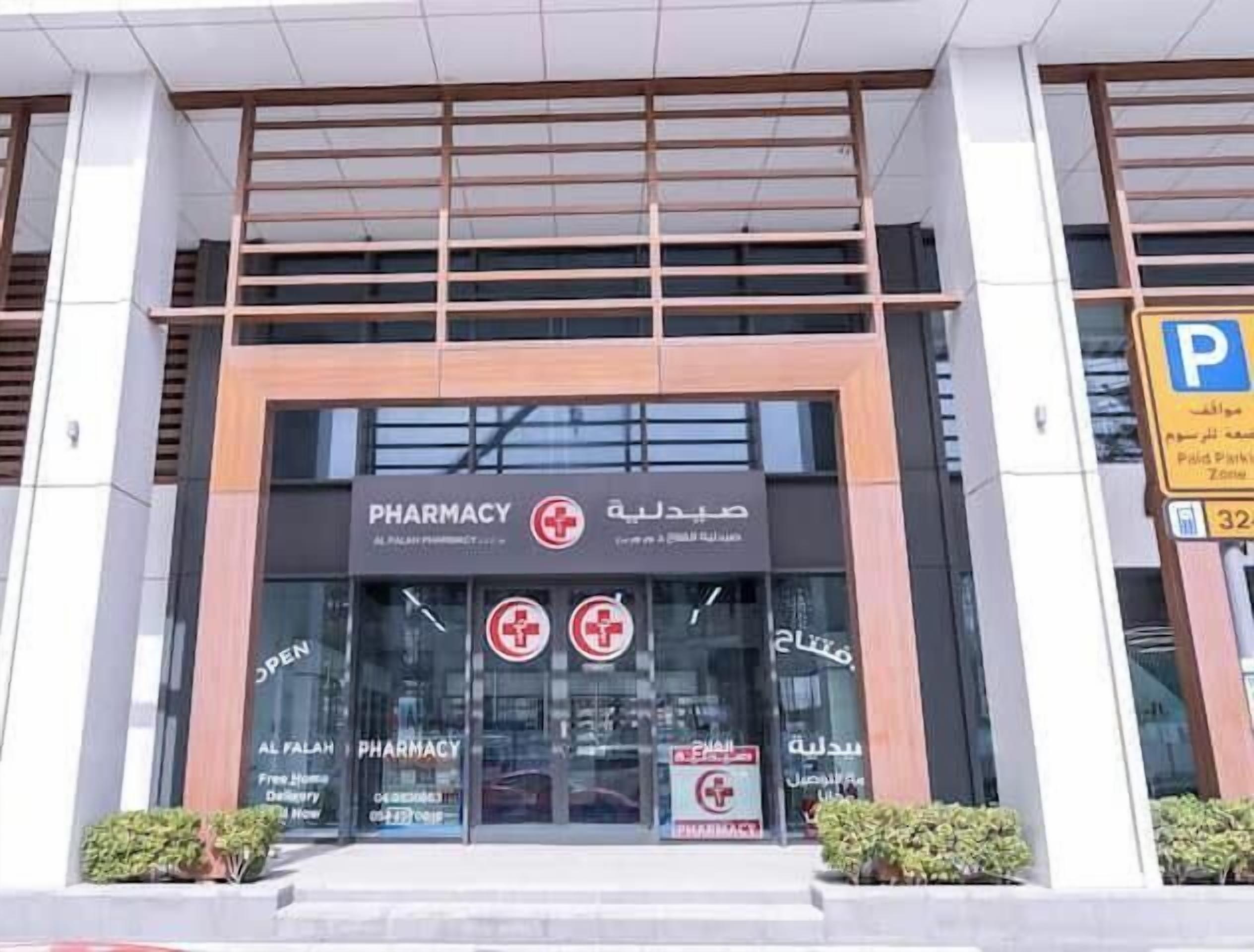 Una farmacia con un letrero en árabe e inglés, entrada de vidrio y señalización de estacionamiento cerca.