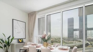 A modern dining room with a large window, a framed abstract artwork, and a dining table set for four. - Vogue | Al Wasl 1 Residence near World Trade Centre (Dubai)