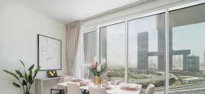 Un comedor moderno con una mesa dispuesta para cuatro, ventanas amplias que ofrecen vistas a la ciudad y una obra de arte abstracta enmarcada en la pared.