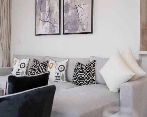 Uma sala de estar com um sofá cinzento, almofadas estampadas e arte abstrata na parede.
