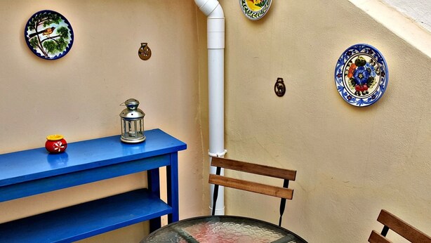 Een kleine kamer met een blauwe tafel, een glazen tafel en een stoel. Er hangen decoratieve borden aan de muur.