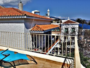 A building with a tiled roof, a balcony with a blue chair, and a view of the sea. - Apartamentos Balcón de Europa (Nerja)