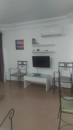 A living room with a flat-screen TV, two metal chairs, a white coffee table, and a cityscape picture on the wall. - Apartamentos Balcón de Europa (Nerja)