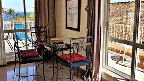 Een kamer met balkon, een tafel met stoelen, een lijst met foto en een airconditioningsysteem.