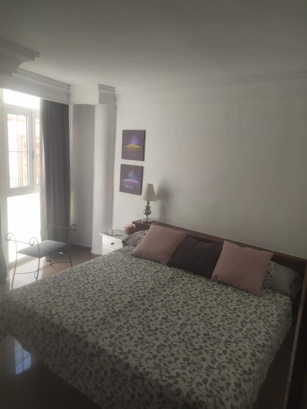 A bedroom with a bed, a nightstand, a lamp, and two wall-mounted pictures. - Apartamentos Balcón de Europa (Nerja)