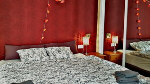 Een slaapkamer met een groot bed, een nachtkastje, een lamp en een spiegel.