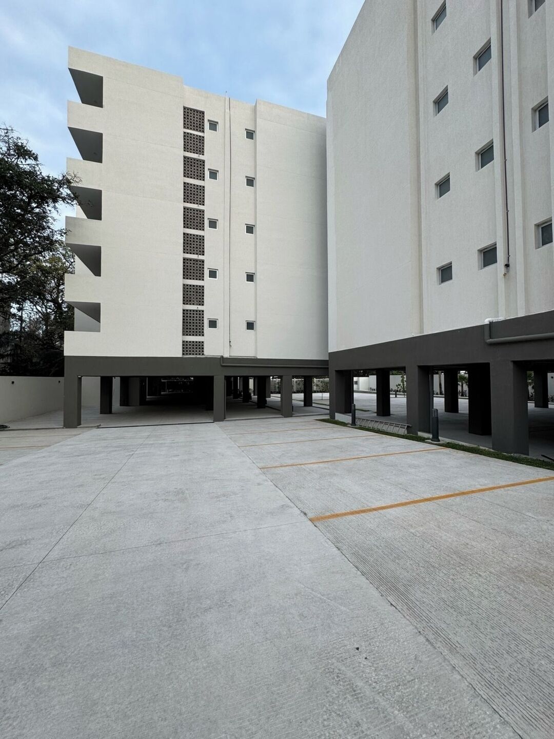 A modern building with a flat facade, multiple floors, and a covered parking area.