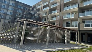 Un immeuble moderne à plusieurs étages, doté de balcons, d’un espace extérieur aménagé et couvert, et d’une clôture à motifs.