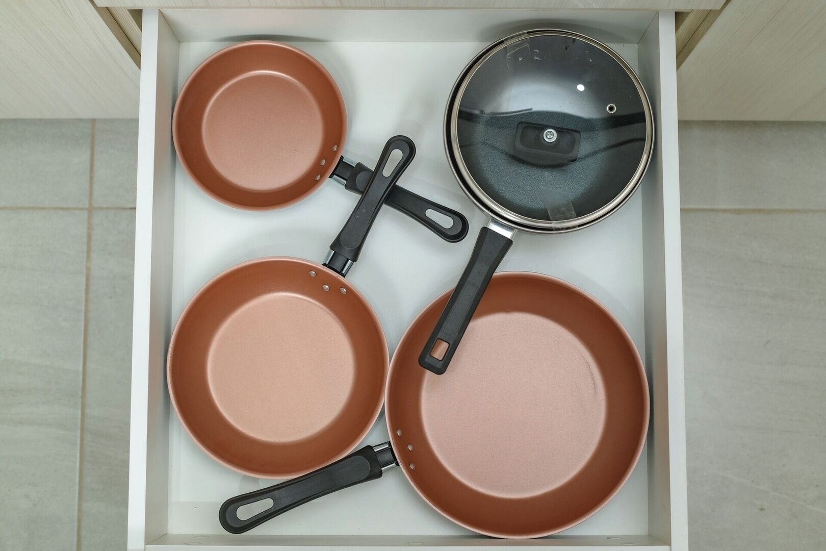 Un tiroir contenant quatre casseroles marron et un couvercle.