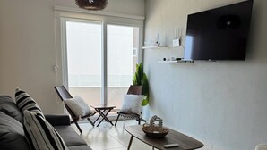 Sala de estar con sofá, sillones, una mesa de centro, televisión y un balcón con vistas.