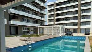 Un edificio de apartamentos moderno con piscina, mobiliario exterior y cochera.