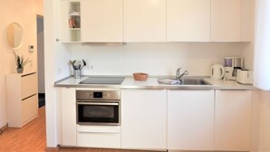 A modern kitchen with white cabinets, a built-in oven, a sink, and a coffee maker. - Ferienwohnung Badnerstraße L4 (Endingen am Kaiserstuhl)