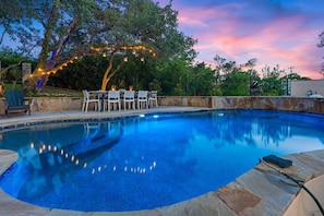 Ein Pool mit einer Steinterrasse, umgeben von Bäumen und einem Tisch mit Stühlen.