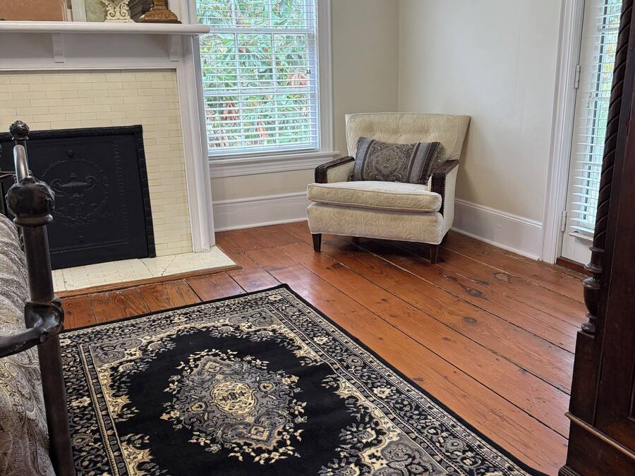 A room with a fireplace, a window with blinds, a patterned rug, and a chair.