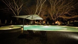 A nighttime outdoor swimming pool with lounge chairs and an umbrella. - Holistic EcoHotel (San Nicolás)