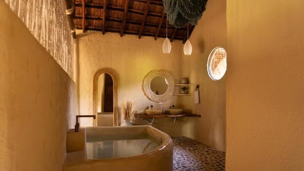 A bathroom with a large bathtub, a round mirror, and a shelf with toiletries. - Holistic EcoHotel (San Nicolás)
