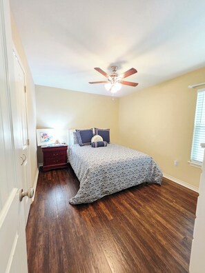 Un dormitorio con cama, cómoda, ventilador de techo y ventana.