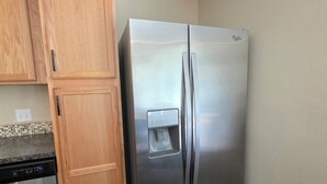 A stainless steel refrigerator with a water dispenser, wooden cabinets, and a dishwasher in a kitchen with dark wooden flooring. - Charming 2-bedroom House Near Rockport's Downtown Cultural District (Rockport)