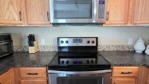 Una cocina con gabinetes de madera, un microondas de acero inoxidable, una estufa a gas y un horno.