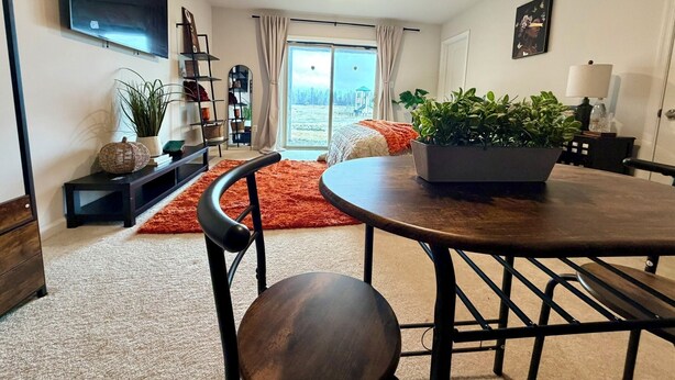 Un salon moderne doté d’un téléviseur à écran plat, d’une table à manger avec des chaises, d’une grande fenêtre avec des rideaux et offrant une vue sur l’extérieur.