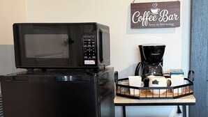Un réfrigérateur noir avec un four à micro-ondes sur le dessus, une machine à café et des récipients étiquetés pour le sucre, le thé et le café.