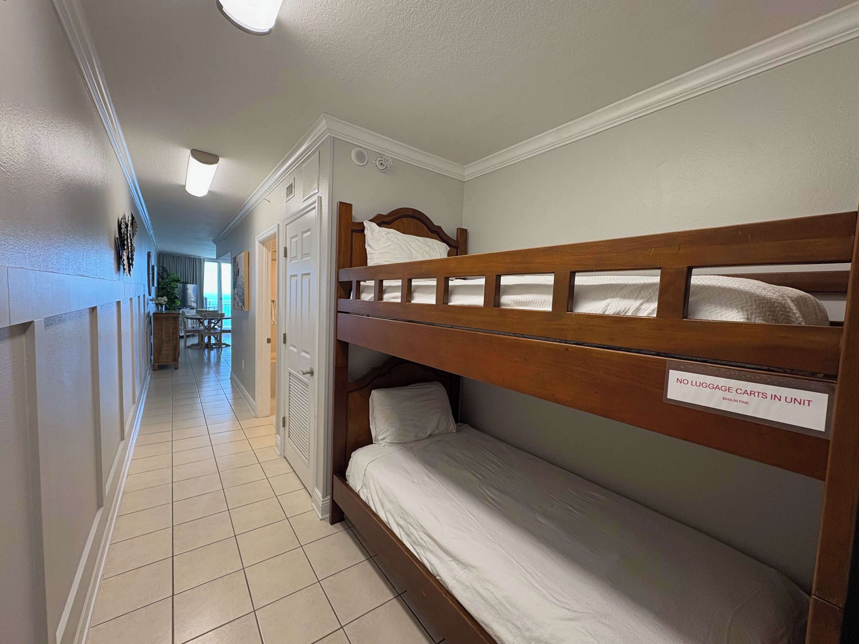 Une chambre d’hôtel avec des lits superposés, un panneau indiquant qu’il n’y a pas de chariots à bagages disponibles dans la chambre, et une vue sur le couloir.